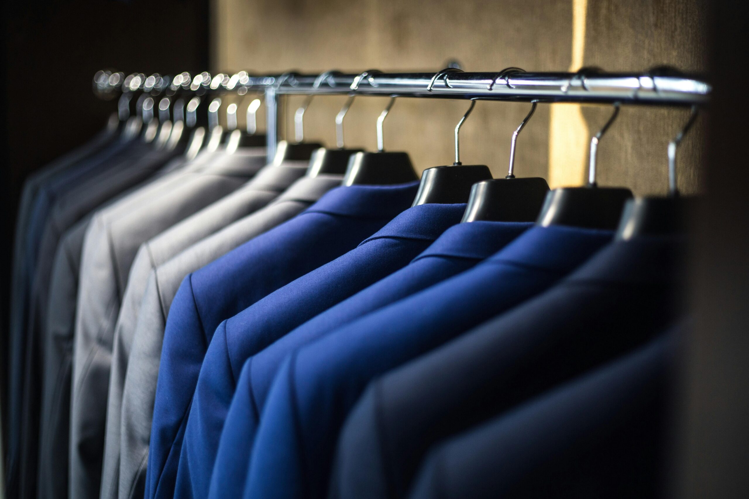 Tailored men's custom suits in blue and gray hanging on a rack.